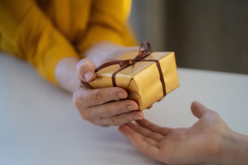 Female hands hold a gift closeup, top view. A young girl gives a nice packed surprise to her mother, grandmother with love, remembers elderly relatives, visits during holidays, takes care of them.